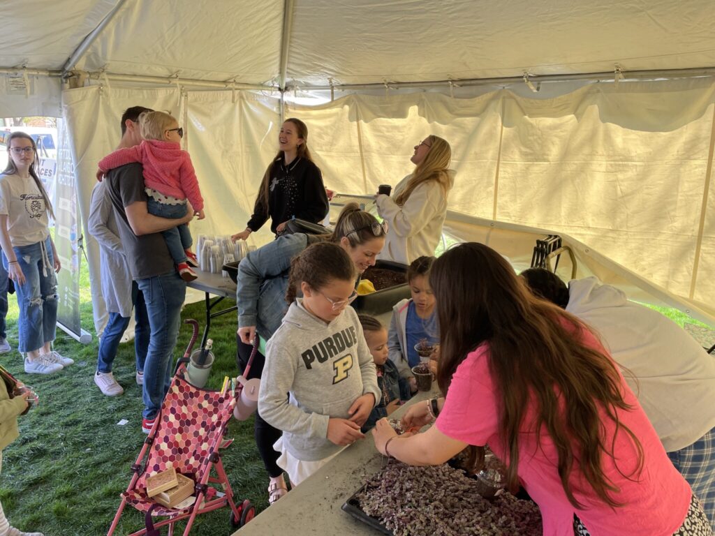 Families lining up to make their plant necklaces while volunteers help out.
