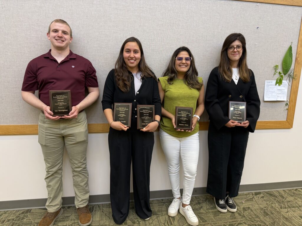 Four individuals holding plaques recognizing achievements at a Purdue HLA awards event.