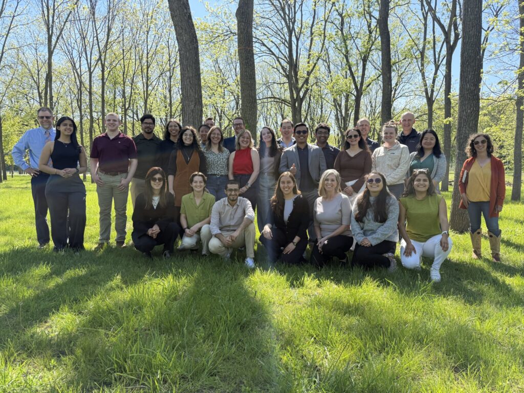 Large group photo of participants outdoors among trees during a research retreat.