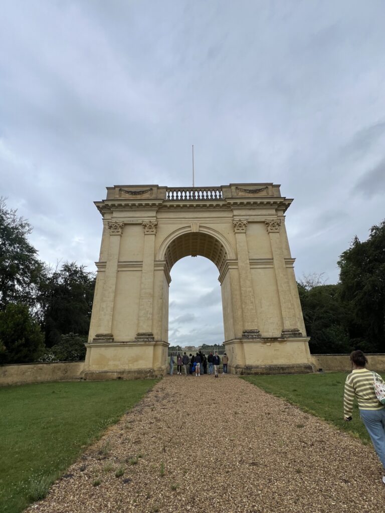 Grand stone archway at Chatsworth Estate with visitors walking beneath it on a gravel path.