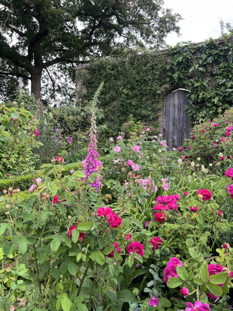 Colorful cottage garden at Sissinghurst featuring roses, foxgloves, and a wooden gate set in a brick wall.
