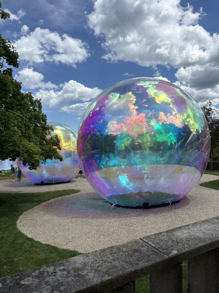 Large iridescent spherical art installations reflect clouds and surrounding gardens at the Chicago Botanic Garden.