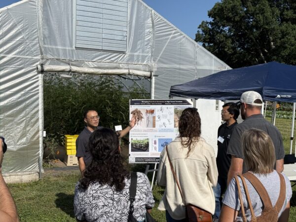 Visitors review research findings presented outside a greenhouse facility.
