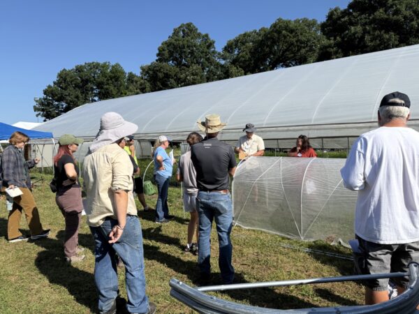 Field day attendees learn about crop protection structures beside a high tunnel.