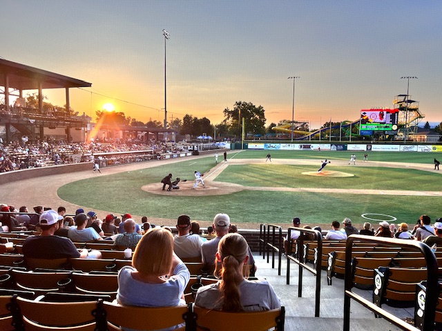 Sunset view of the Prospect League All-Star Game at the Lafayette Aviators stadium, with players on the field and fans filling the stands.