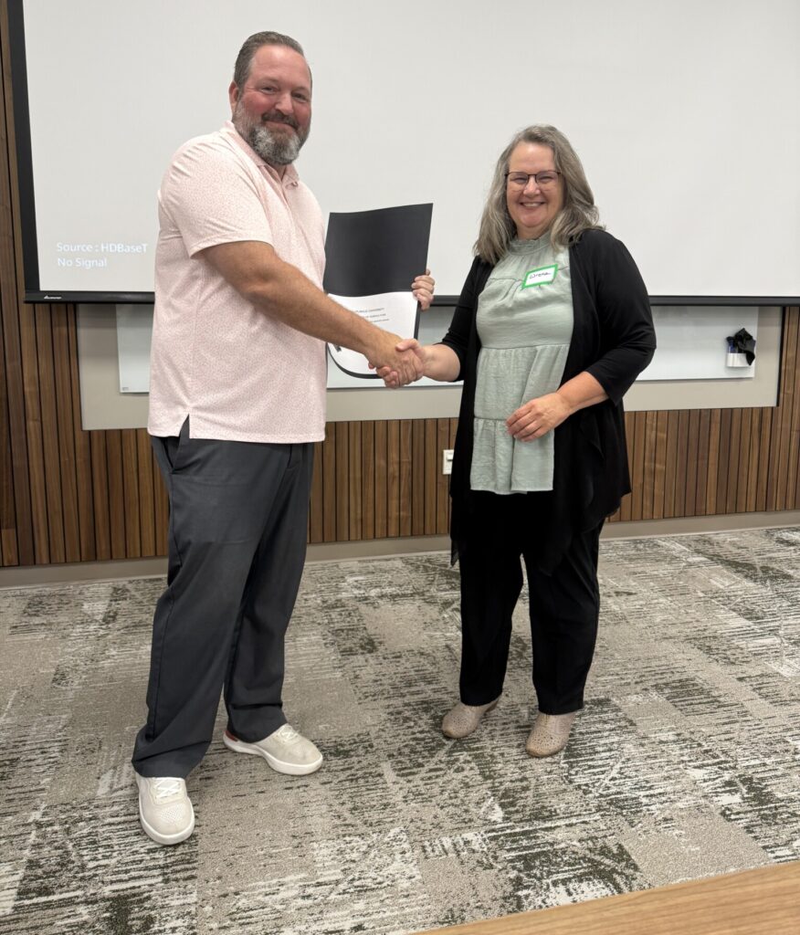 Wrena Hufford, Business Office Clerk, receives a College of Agriculture Business Office Award during a recognition ceremony. Wrena shakes hands with a presenter while holding a certificate.
