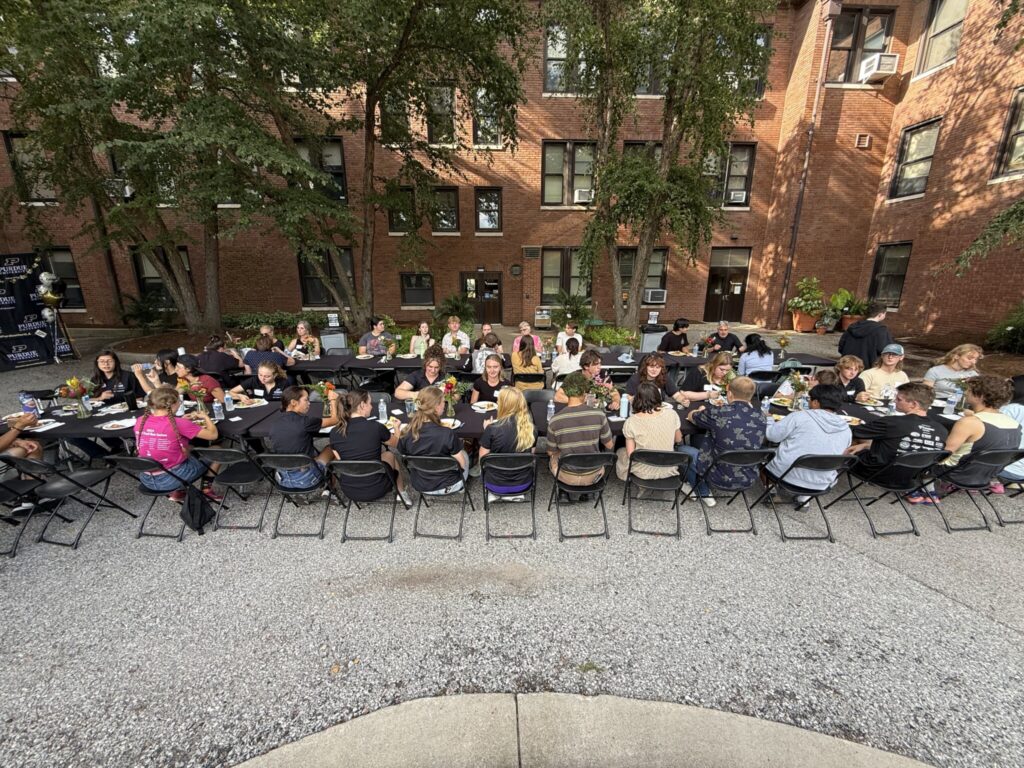 Students, faculty, and staff seated at long tables during an outdoor welcome dinner in a Purdue courtyard.