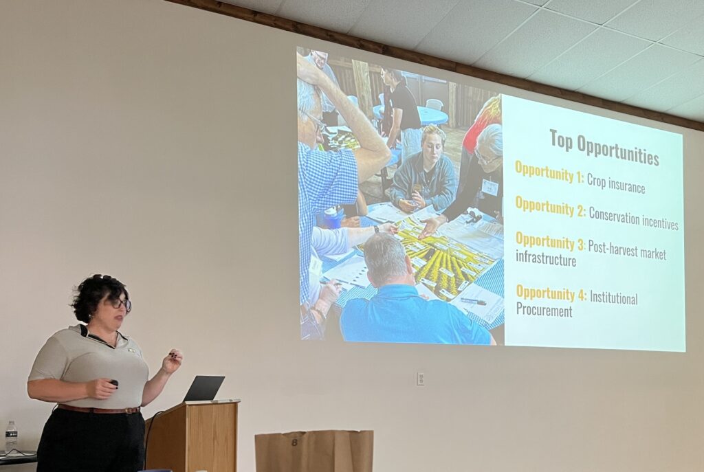 Emily DeaKyne delivers a talk indoors while a slide showing agricultural development opportunities is projected on a screen behind.