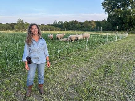Moriah Bilenky stands near a fenced grazing area while sheep feed in a cover-cropped field.