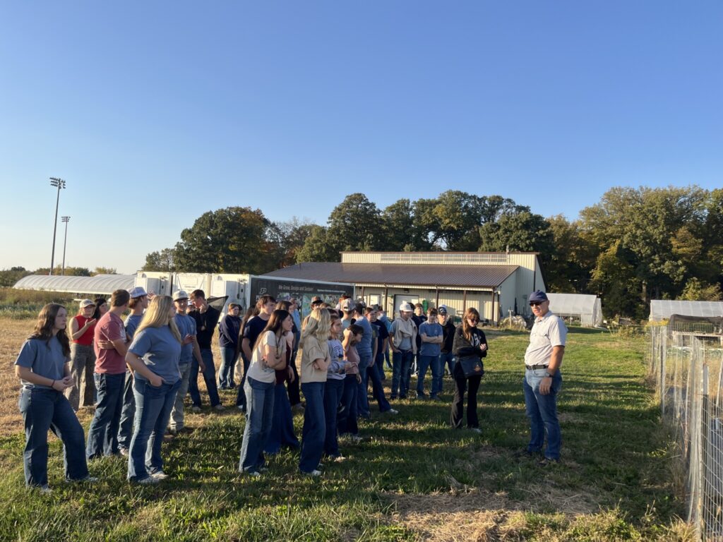 A group of students gathers outdoors for a guided tour of Purdue agricultural research facilities.