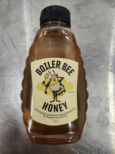 A squeeze bottle of Boiler Bee Honey with a cartoon bee mascot on the label. Text reads: "Proceeds support Bee Research at Purdue University."