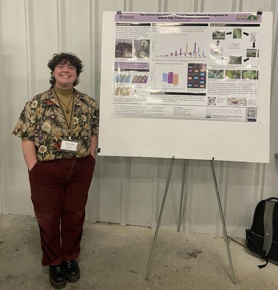 A student stands beside a research poster presentation at a professional conference.