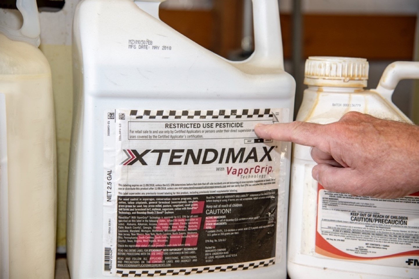 Pesticide product with a hand pointing out the warning label "Restricted Use Pesticide".