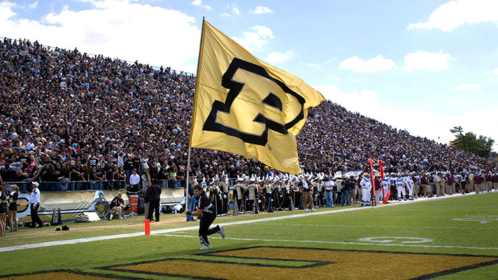 Purdue University student running with Purdue flag on football field.