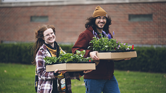 Two people carrying plants at the Purdue Extension Master Gardener plant sale.