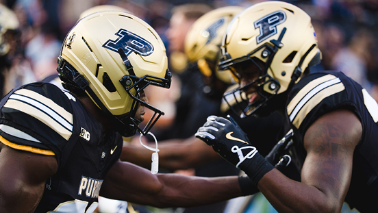 Purdue football players celebrating in gold helmets on the field.