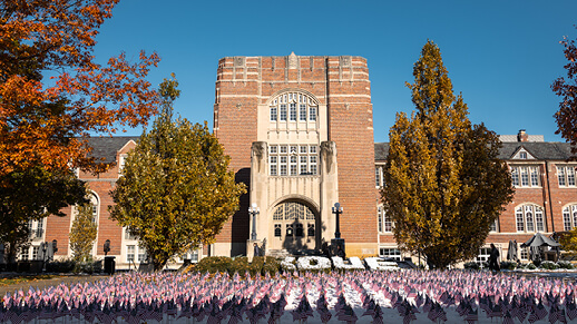 Purdue University building on a clear autumn day with a field of small American flags arranged on the lawn in front.