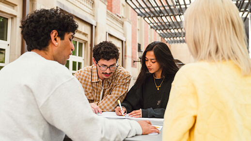 Group of four students sitting around an outdoor table together and studying.