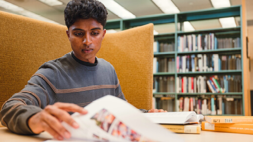Student seated in a library booth flipping through a textbook.