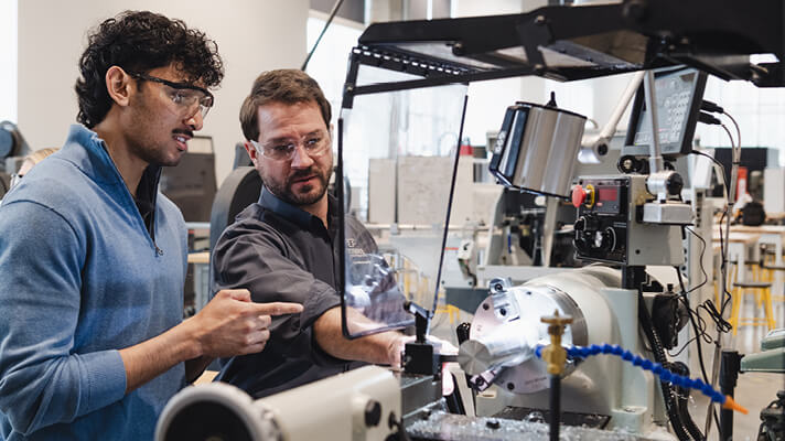 Instructor and student inspecting precision machinery in an engineering lab.
