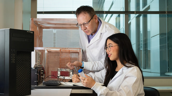 Researcher and student examining lab equipment together in a laboratory setting.