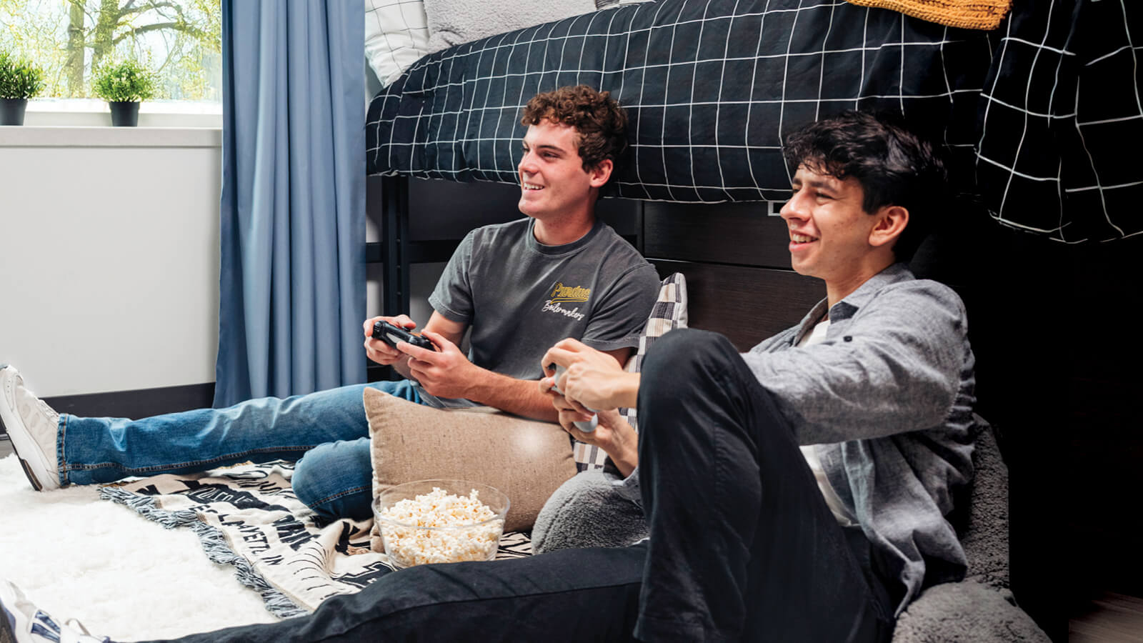 Two students sitting on the floor of a dorm room playing video games.