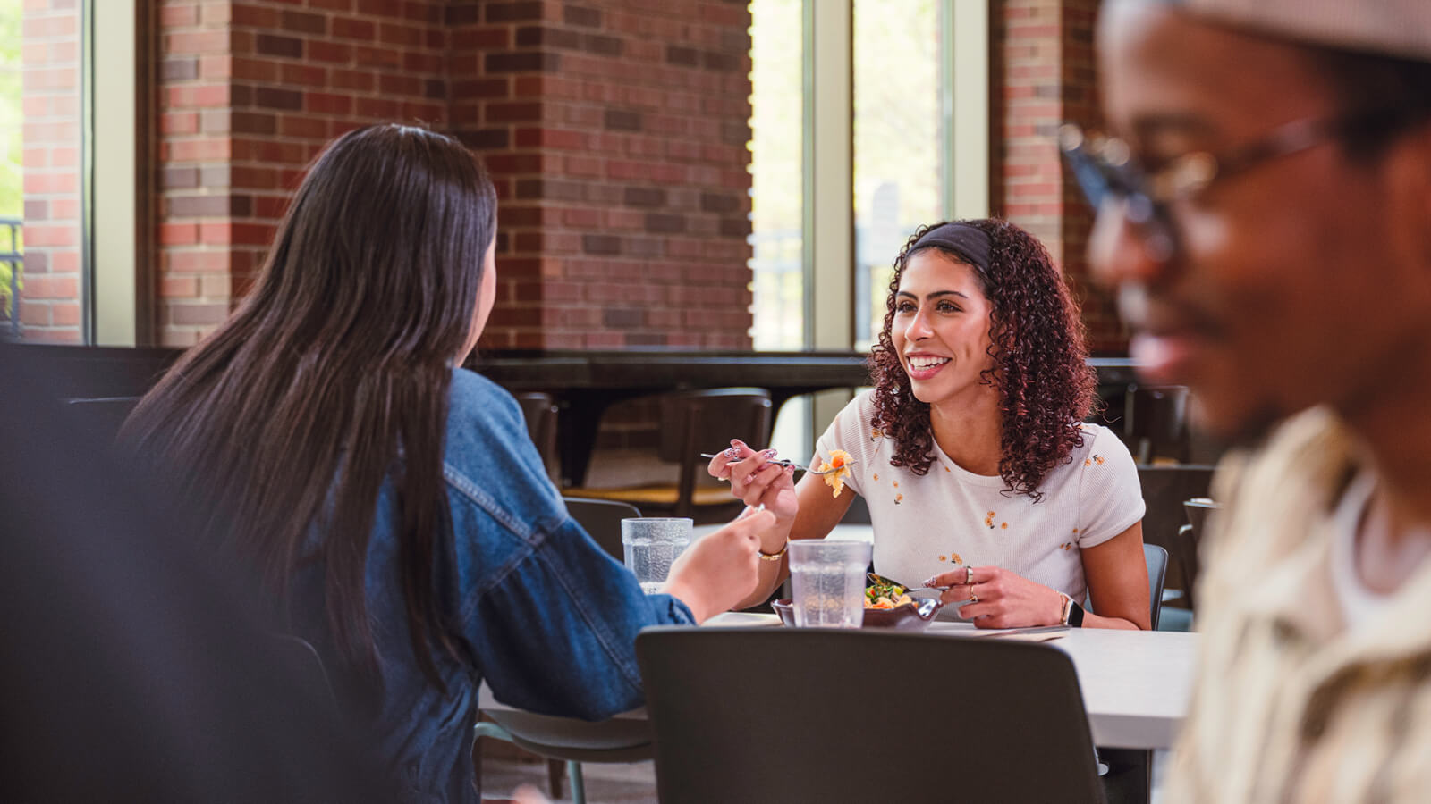Two students sitting across from each other and eating in a dining hall.