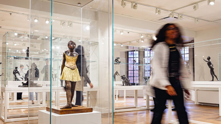 Visitor walking past a sculpture display case inside an art gallery.