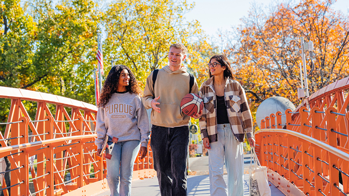 Alt text: Three Purdue students walking on a bridge.  