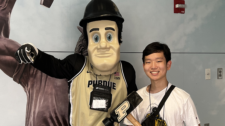 Young man smiling with mascot while holding Purdue hammer.