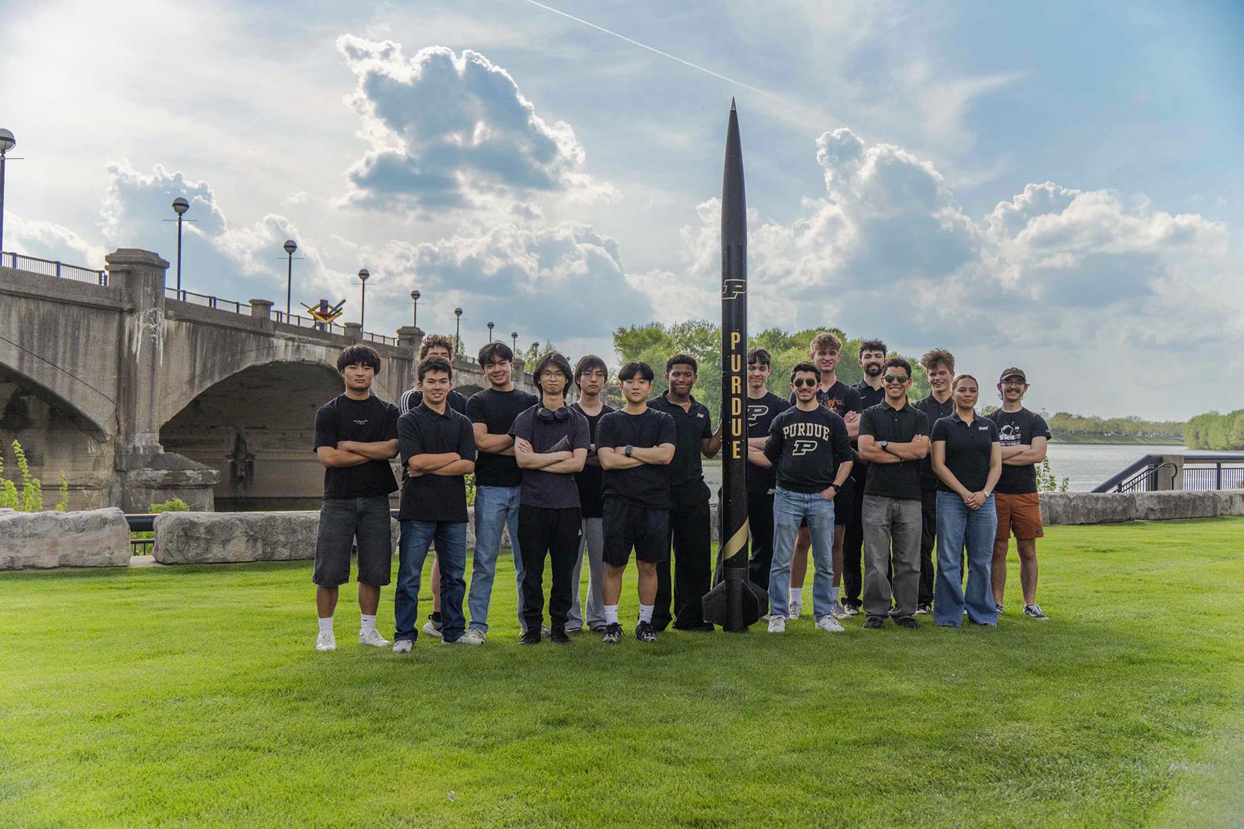 A group of students stand around a large rocket on a grass field