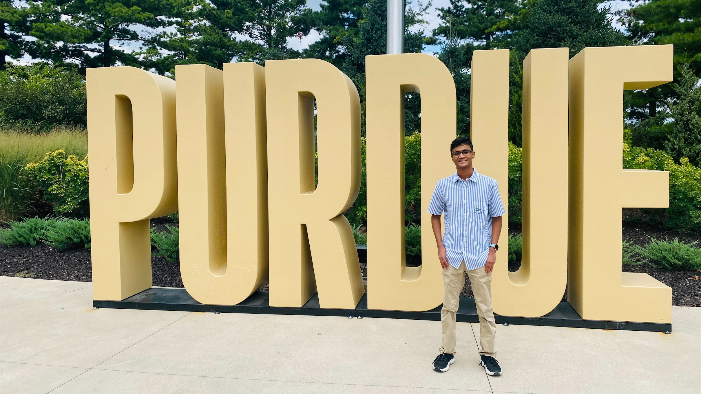 A young man smiling next to a Purdue sign at a campus entrance.