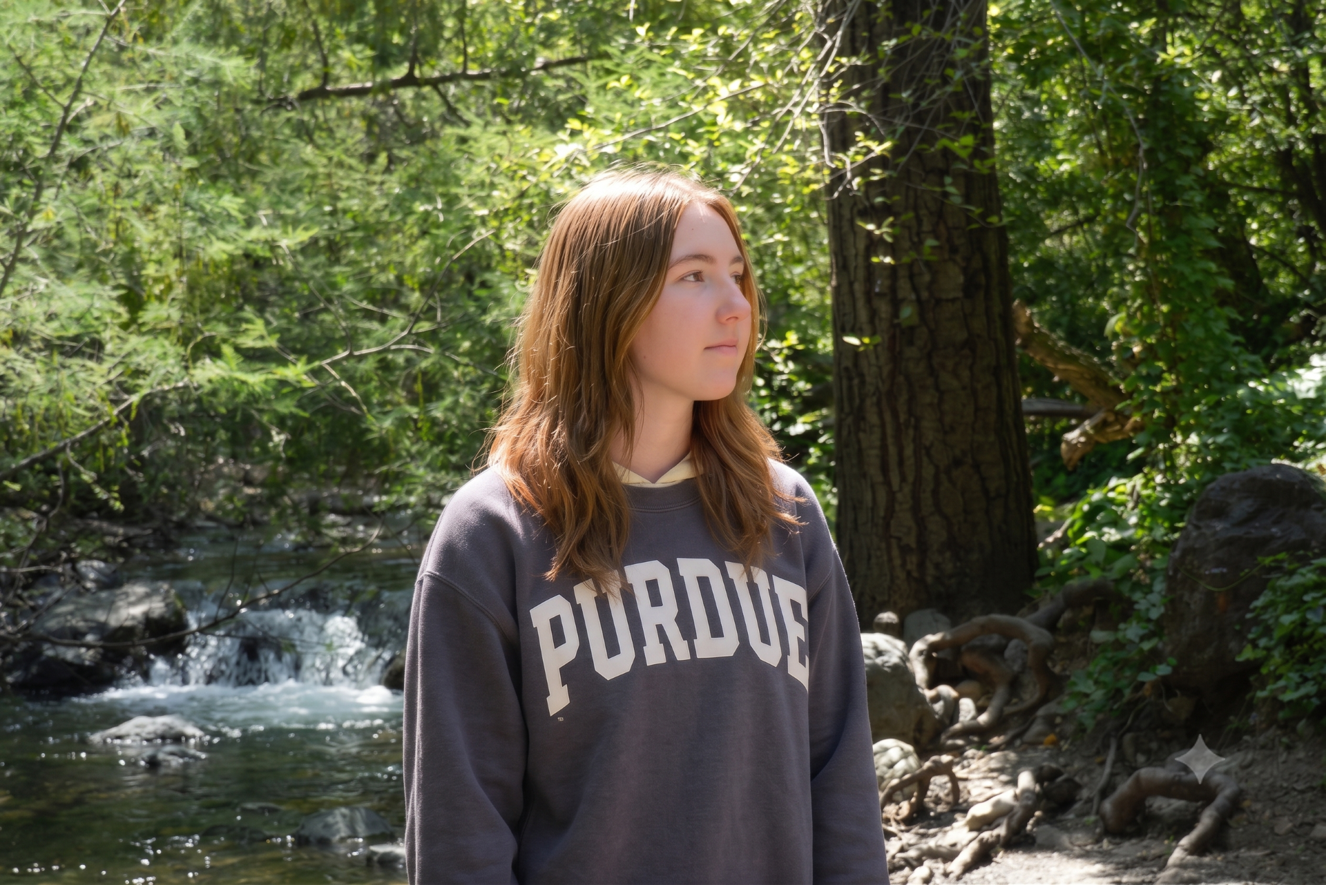 A young woman wearing a Purdue shirt with the forest and a creek behind her