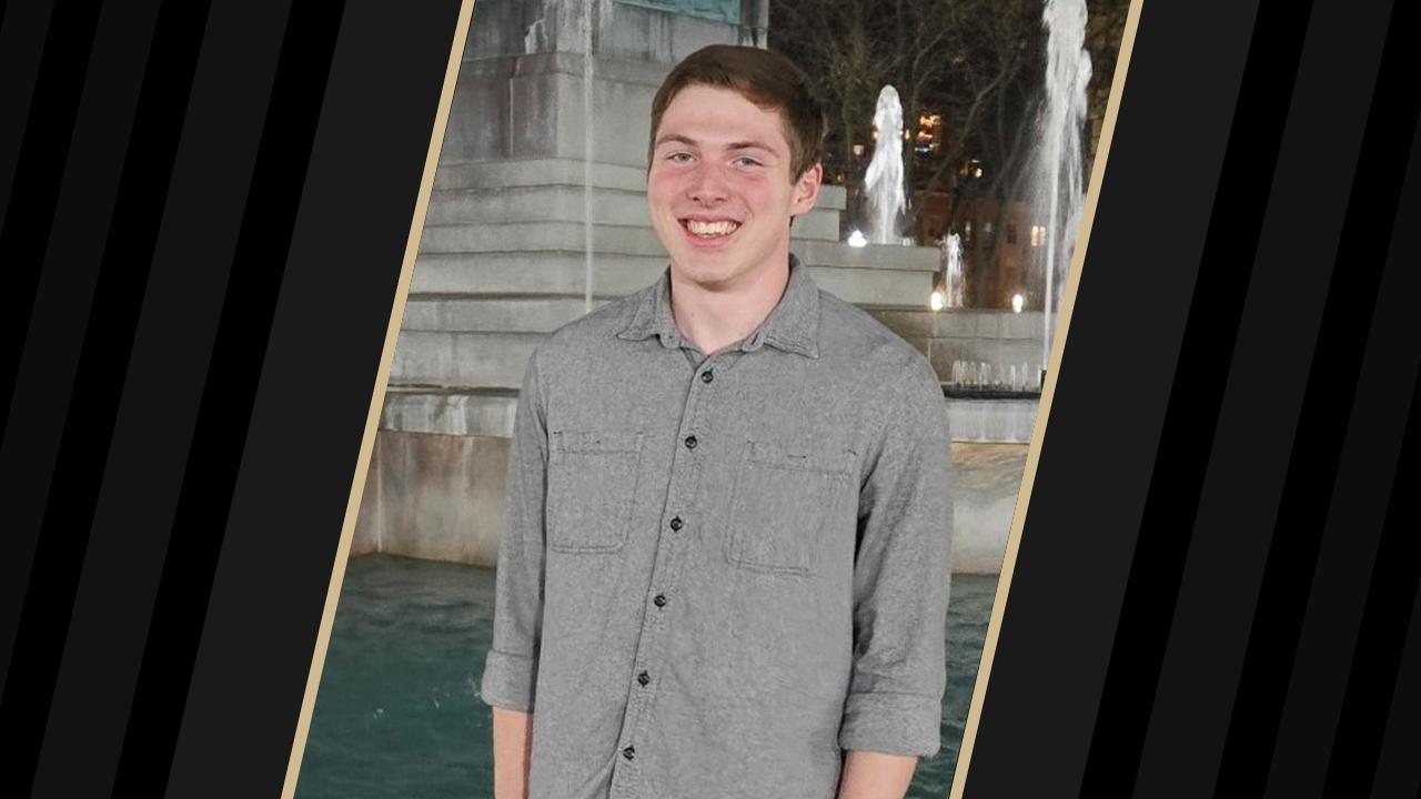 Student wearing a gray shirt standing in front of a fountain