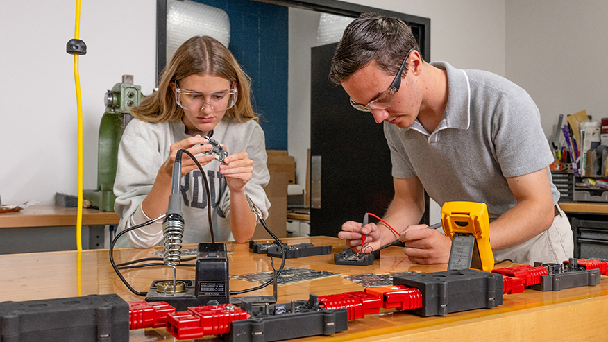 Two students working on circuit hardware using tools