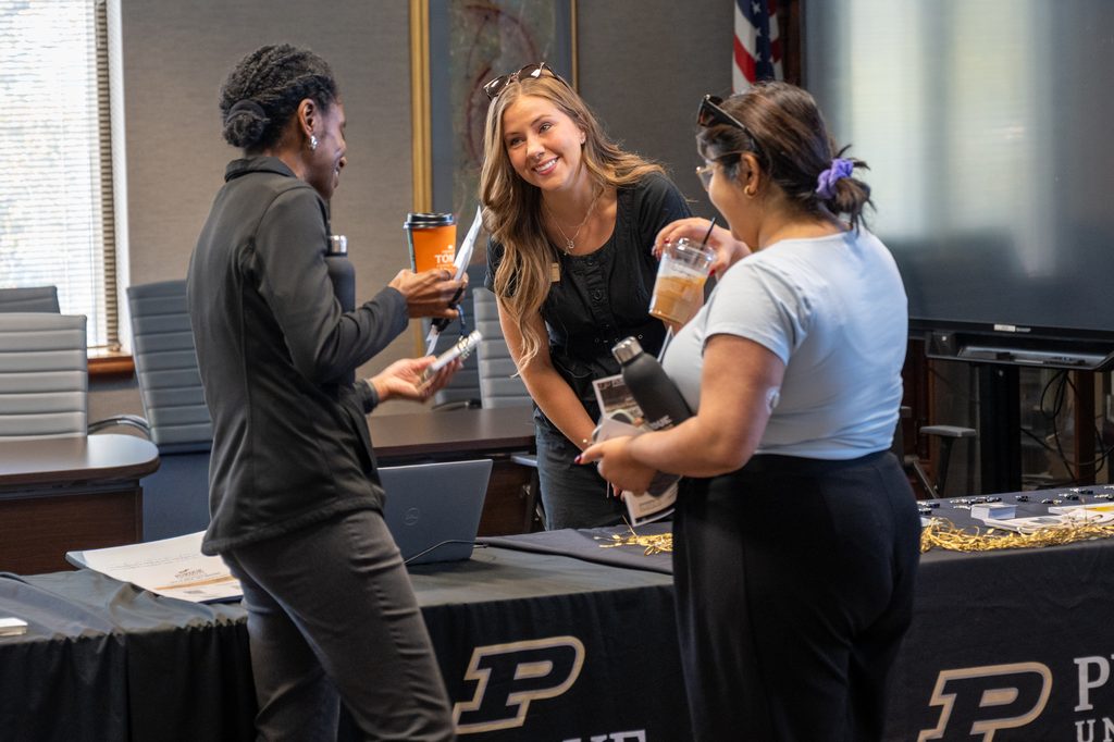 Three event attendees talk near a Purdue-branded registration table.