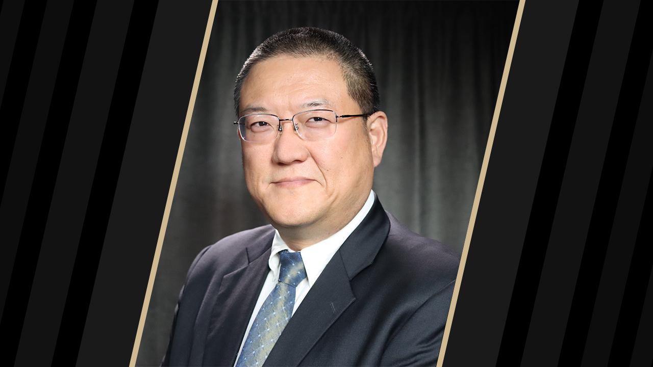 Headshot of a man wearing glasses and a suit with black borders