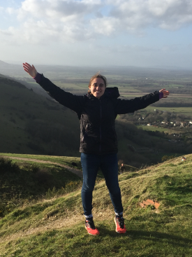 Marie Armes spreads her arms wide and smiles while hiking in the countryside