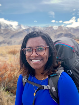 Sohinee Bera wears a hiking backpack in a scenic background while hiking in New Zealand
