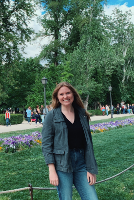 Violet Kuchta stands in a park in Amsterdam with purple flowers and people in the background