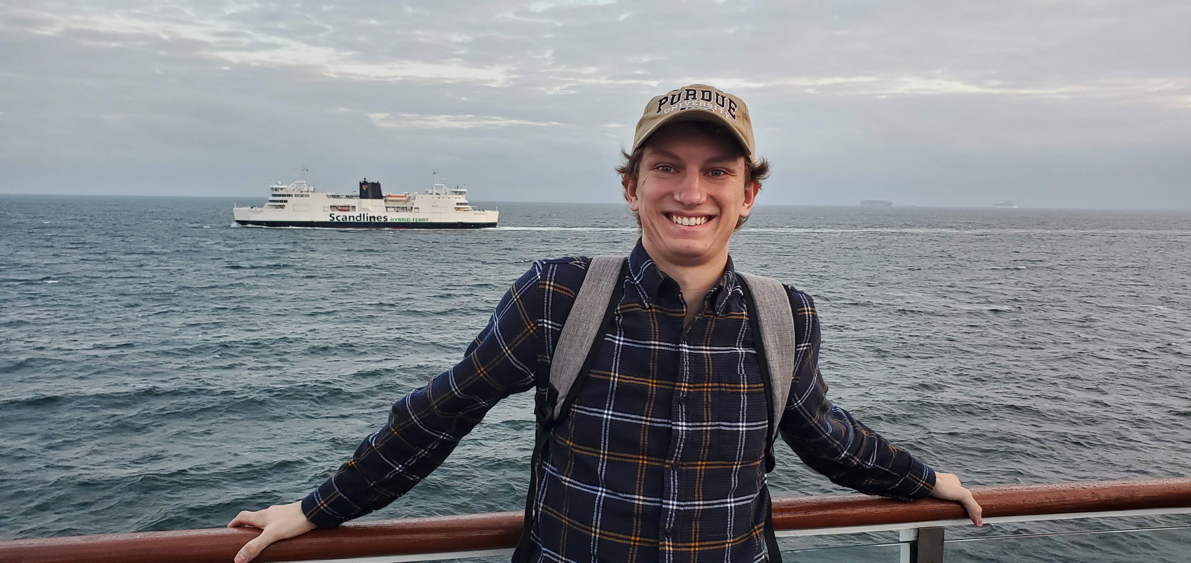 Dan English stands by the rail of a ship with ocean and another ship in the background