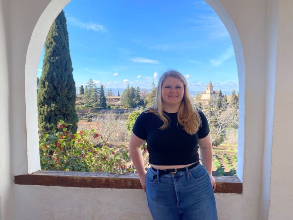 Holly Shaver stands in front of an arched window with scenic garden background