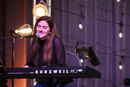 Kelsey singing and playing the keyboard at a songwriter's event