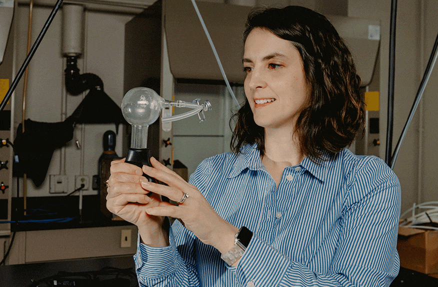 A Purdue professor stands in her lab, holding a glass “cloud in a bottle” demonstration