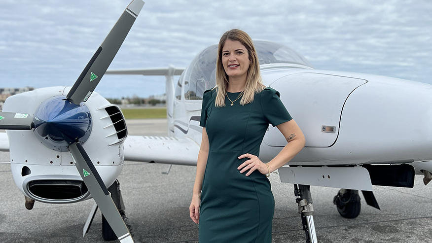 Purdue Global professor Marisa Aguiar stands between the nose and propeller of a small airplane.