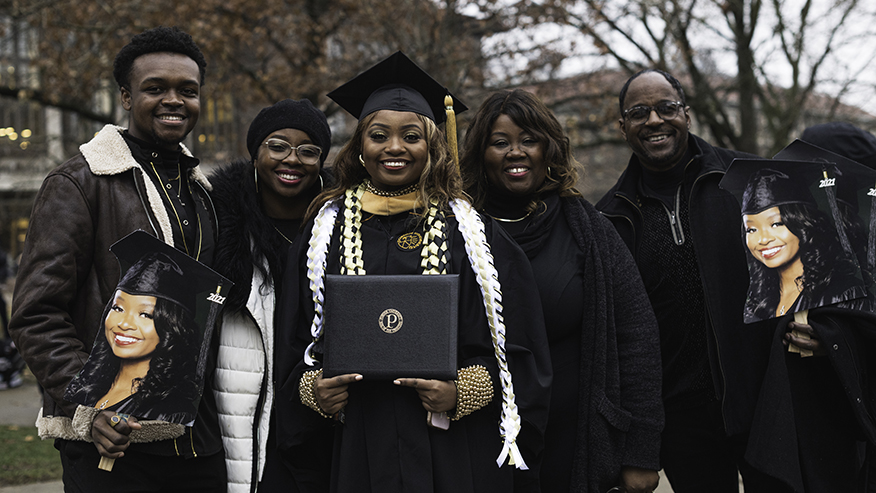 A student graduating from Purdue University poses with family members outside Elliott Hall of Music.