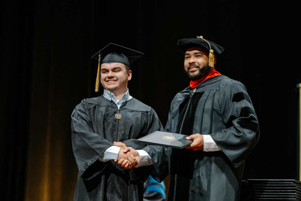 Purdue Global graduate Chris Huber shakes hands with Julius Keller while receiving his degree at commencement.