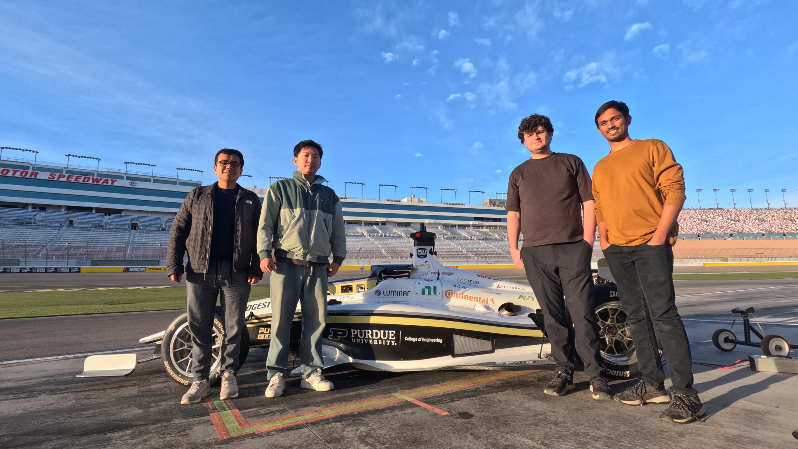 Four young people surround race car at a motor speedway