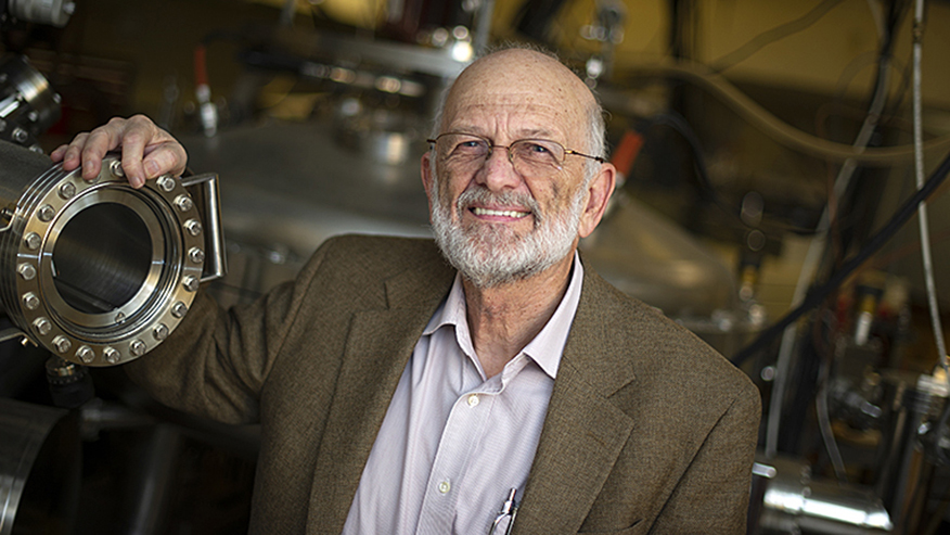 Man with gray beard smiling next to machine