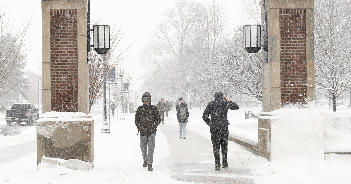 Students walk between brick pillars on a snowy day at Purdue University.
